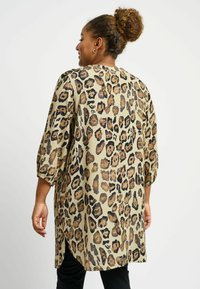 Tunika s uzorkom leopard u bež i smeđoj boji, sa opuštenim krojem, rukavima do tri četvrtine i blago zakrivljenim rubom. Glatka tekstura tkanine.