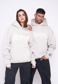 Le felpe grigie chiare presentano una tasca frontale e un audace logo "Multiply". Indossate con pantaloni cargo neri, che mostrano un look e una vestibilità rilassati.
