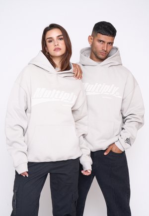 Le felpe grigie chiare presentano una tasca frontale e un audace logo "Multiply". Indossate con pantaloni cargo neri, che mostrano un look e una vestibilità rilassati.