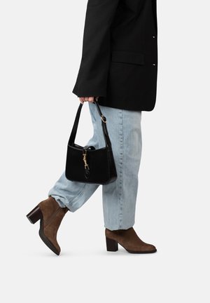 Sac en cuir noir avec des détails de fermeture éclair dorés, associé à un jean en denim bleu clair et des bottines en daim marron à talons carrés.