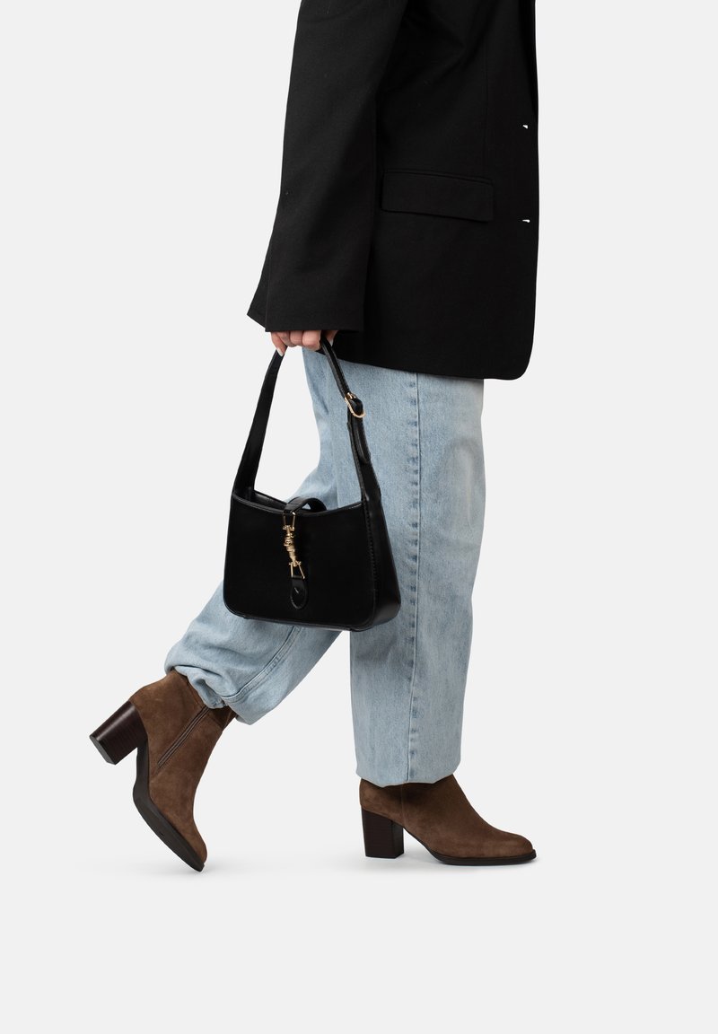 Borsa a tracolla in pelle nera con dettagli in oro, abbinata a jeans in denim azzurro e stivaletti in suede marrone con tacco a blocco.