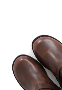 Botas de cuero marrón con un acabado suave, punta redonda y detalles cosidos a lo largo de la suela. La superficie muestra una textura rica.