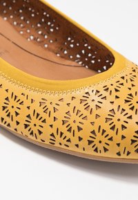 Zapatos planos de cuero amarillos con patrones florales recortados, punta redonda y borde cosido. El interior presenta un forro marrón suave.