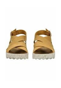 Hnědé kožené sandály s kříženými pásky, texturovanou bílou podrážkou a zapínáním na přezku kolem kotníku; otevřená špička, moderní tvar.