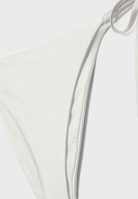 Bas de bikini blanc avec fermetures à nouer sur les côtés, présenté sur un fond uni, mettant en évidence la texture du tissu et les détails des coutures.