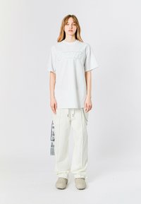 Camiseta blanca de gran tamaño con un logo reflectante, combinada con pantalones cargo blancos con bolsillos laterales y un estampado gráfico. Calzado texturizado.