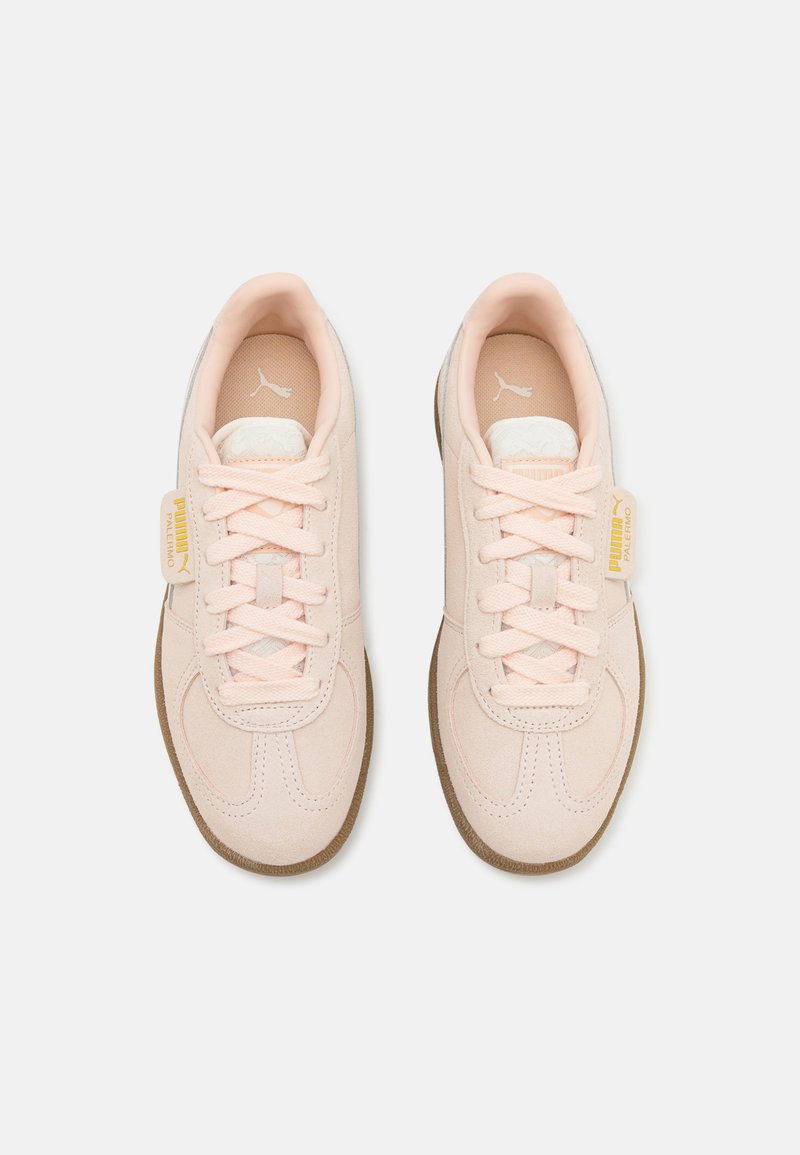 Baskets en suède rose clair avec des lacets blancs, des détails de couture subtils et des semelles en caoutchouc gomme. Présente une petite étiquette de marque jaune sur le côté.