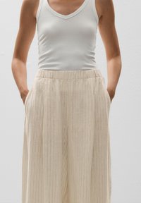 Lightweight, elastic waistband, cream-colored trousers with subtle vertical stripes and side pockets. Smooth, soft fabric texture.