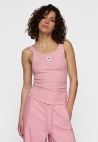 Lichtroze geribbelde tanktop met brede banden en een vierkante logopatch op de borst, gecombineerd met bijpassende roze joggingbroek met trekkoord.