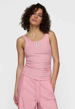 Lichtroze geribbelde tanktop met brede banden en een vierkante logopatch op de borst, gecombineerd met bijpassende roze joggingbroek met trekkoord.