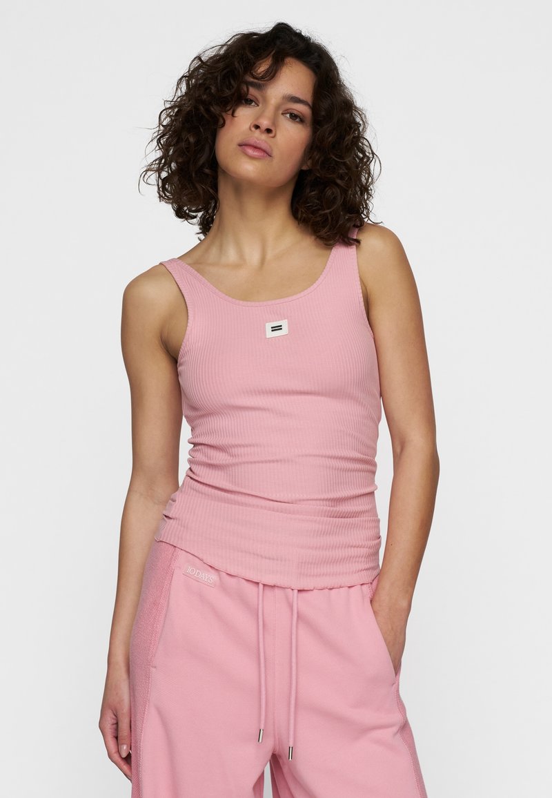 Lichtroze geribbelde tanktop met brede banden en een vierkante logopatch op de borst, gecombineerd met bijpassende roze joggingbroek met trekkoord.