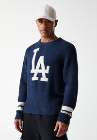 Suéter marinero con logo blanco "LA", tejido texturizado, puños y dobladillo acanalados. Combinado con una gorra gris claro con bordado del logo.