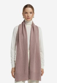 Jasnoróżowy dziany szalik z prążkowanym wykończeniem, wykonany z miękkiego materiału. Otula szyję, doskonale uzupełniając biały golf.