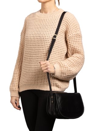 Borsa a spalla nera in pelle con pattina pieghevole, bordi testurizzati e una tracolla regolabile, tenuta da una persona che indossa un maglione lavorato a maglia beige.