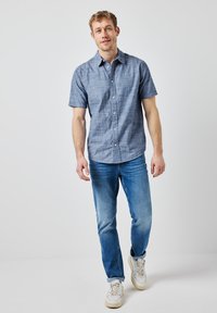 Kortärmad knäppskjorta i ljusblått tyg med ett subtilt rutmönster, matchad med ljusblå jeans och vita sneakers.