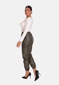 Witte lange mouwen top met geplooide details, gecombineerd met olijfgroen faux leren joggers met elastische manchetten en zijzakken. Zwarte stiletto hakken.