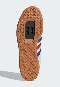 Soletta di sneakers bianche con una suola in gomma marrone testurizzata. Presenta un meccanismo a clip nero e strisce rosse e blu sui lati.
