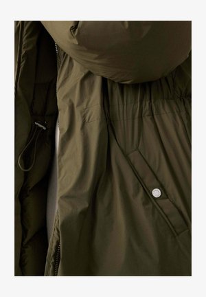 Veste matelassée vert olive foncé avec capuche, fermeture éclair, taille élastique et détail à bouton-pression sur le côté. Texture douce et lisse.