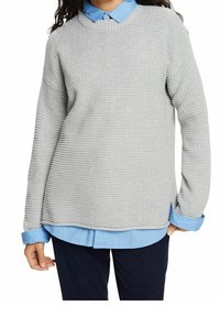 Grijze gestructureerde trui met lange mouwen, ronde halslijn en zijsplitten, gelaagd over een blauwe blouse met kraag.