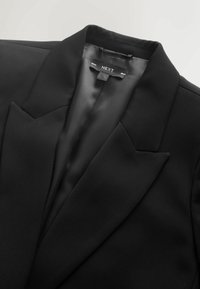 Schwarzer Blazer mit satinierter Innenausstattung, Reverskragen und einer einzelnen Brusttasche. Etikett lautet "NEXT." Glatte Textur und strukturiertes Design.