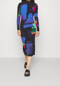 Femme marchant dans une robe midi noire à manches longues avec des motifs abstraits colorés, portant des sandales à plateforme noires.