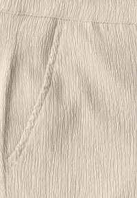 Ljusbeiga textured byxor med ribbad yta, som har en sidficka och en elastisk midja. Materialet verkar mjukt och ventilerande.