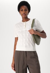 White short-sleeve sweater with a cable knit pattern, ribbed hem, and three-button placket. Paired with olive green handbag.