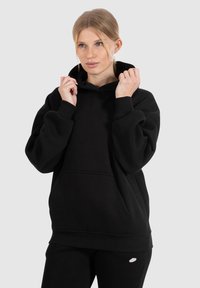 Hoodie noir avec poche kangourou, capuche à cordon de serrage, poignets côtelés et texture douce ; associé à un pantalon noir assorti.
