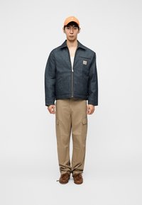 Τζιν μπουφάν με φερμουάρ μπροστά, τσέπη στο στήθος και σκουρόχρωμο πλύσιμο. Συνδυάζεται με χακί παντελόνι cargo και καφέ παπούτσια. Πορτοκαλί καπέλο στο κεφάλι.