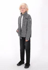 Sivi zip-up jakna s visokim ovratnikom i bočnim džepovima, izrađena od teksturirane tkanine. Uparen s crnim hlačama i crnim cipelama.