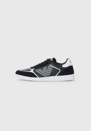 Zwart-witte low-top sneaker met een vleugellogo aan de zijkant, witte zool, zwarte veters en een witte merkheel tab.