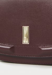 Borsa in pelle bordeaux con finitura testurizzata, dotata di un accentuato accessorio in oro a forma rettangolare e cuciture dettagliate lungo i bordi.