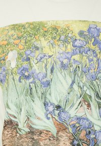 Valkoinen T-paita, jossa on värikäs kukkakuosi; pääasiallisesti violetteja iiriksiä ja oransseja kukkia vihreällä, maanläheisillä sävyillä taustalla.