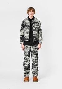 Chaqueta y pantalones abstractos en blanco y negro, hechos de una tela texturizada. Combinados con una blusa negra y zapatos marrones.