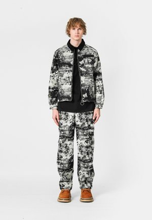 Chaqueta y pantalones abstractos en blanco y negro, hechos de una tela texturizada. Combinados con una blusa negra y zapatos marrones.