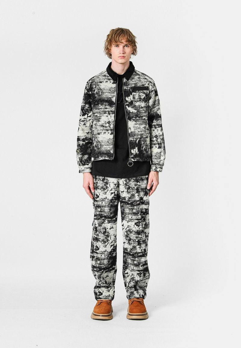 Chaqueta y pantalones abstractos en blanco y negro, hechos de una tela texturizada. Combinados con una blusa negra y zapatos marrones.