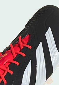 Scarpino da calcio nero con lacci e dettagli rossi. Presenta tre strisce argento prominenti, superficie testurizzata e un design aerodinamico.