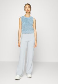 Suéter cropped em malha de cabos azul claro com design sem mangas, combinado com calças largas felpudas de cintura alta azul claro e ténis brancos.