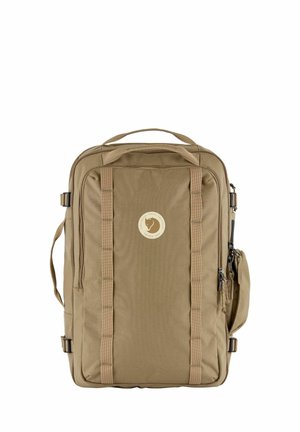 Rechteckiger hellbrauner Reise-Rucksack mit oberem Griff, seitlichem Gurt, vorderen Schlaufen und rundem Logo in der Mitte auf weißem Hintergrund.