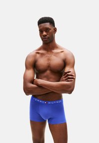 Boxer de algodón azul con un diseño ajustado y una cintura elástica que lleva el nombre de la marca "TOMMY HILFIGER" en texto blanco.