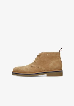 Hellbrauner Wildleder-Stiefelette mit drei Ösen zum Schnüren, rundem Zehenbereich, genähter Sohle mit blauer Biese und Zuglasche an der Rückseite.