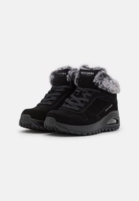 Zapatos deportivos de ante negro con un cuello de pelo sintético, diseño de cordones y suela de goma texturizada con detalle de amortiguación de aire.