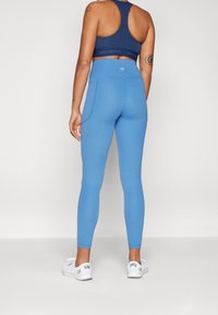 Niebieskie legginsy wykonane z elastycznego materiału, z wysokim stanem. Połączone z ciemnoniebieską koszulką sportową i białymi trikami.
