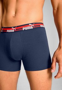 Navy boxer shorts with a branded elastic waistband featuring red and white stripes. Made from a stretchable cotton blend for comfort.