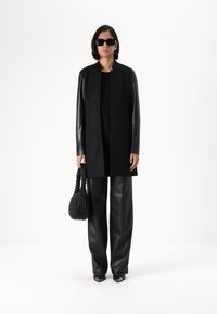 Black structured coat with leather sleeves, paired with wide black leather pants. Accessorized with a woven black handbag and sunglasses.