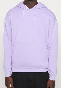 Světle levandulová mikina s kapucí vyrobená z měkké látky. Obsahuje přední kapsu na zip, kapuci na šňůrku a žebrované manžety. Uvolněný střih s hladkou texturou.