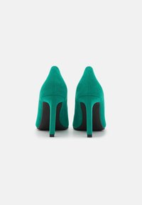 Scarpe col tacco altissimo in suede verde con punta affusolata e tacchi a stiletto sottili. La vista posteriore mostra una trama liscia e una finitura morbida.