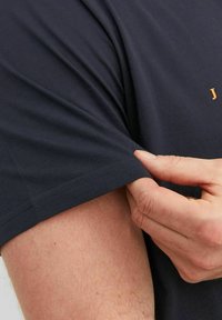 Donker marineblauw katoenen T-shirt met korte mouwen, met een ronde halslijn en een klein oranje logo op de borst. Glad textuur, getailleerde stijl.