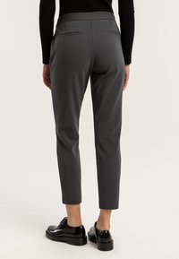 Szare spodnie o eleganckim fasonie, z gładką teksturą, dopasowane, z dwoma tylnymi kieszeniami. W połączeniu z czarnymi butami, o krótkiej długości.