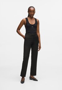 Μαύρη ριγέ αμάνικη μπλούζα με στρογγυλή λαιμόκοψη, συνδυασμένη με μαύρες κομμένες παντελόνες. Το στυλ διαθέτει επίπεδο μπροστινό μέρος και ίσια γραμμή. Μαύρα μαξιλαροειδή παπούτσια με τρουκς.